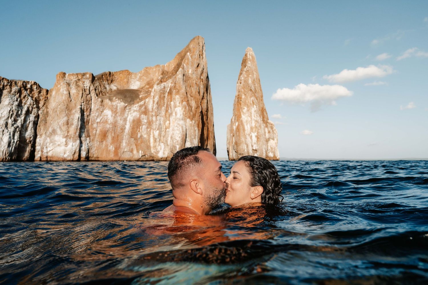 Couple swimming near dramatic rock formations at Percé Rock in Quebec during sunset with golden cliffs in background.