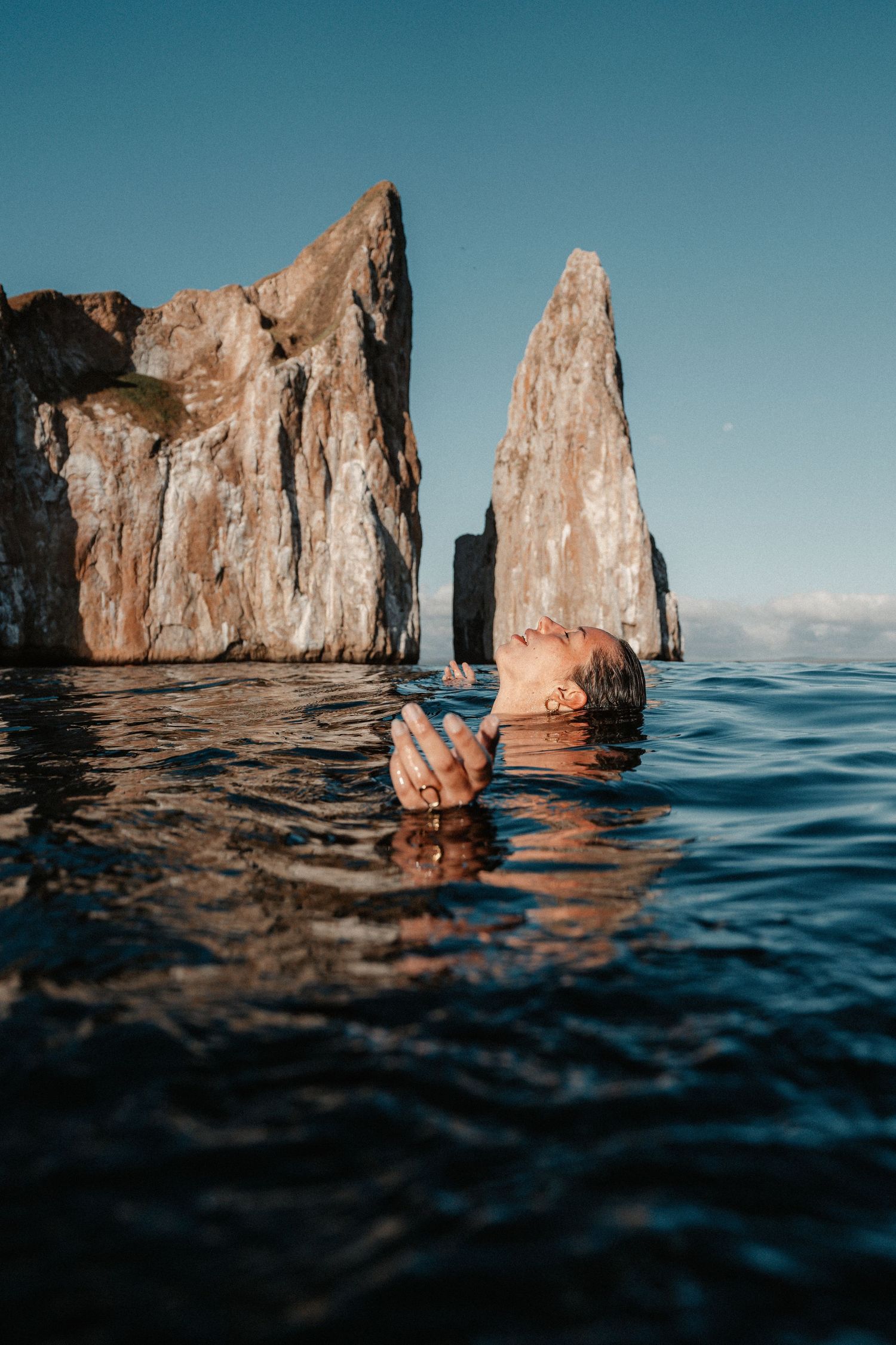 Dramatic rock formations rising from the ocean surface against a clear blue sky.