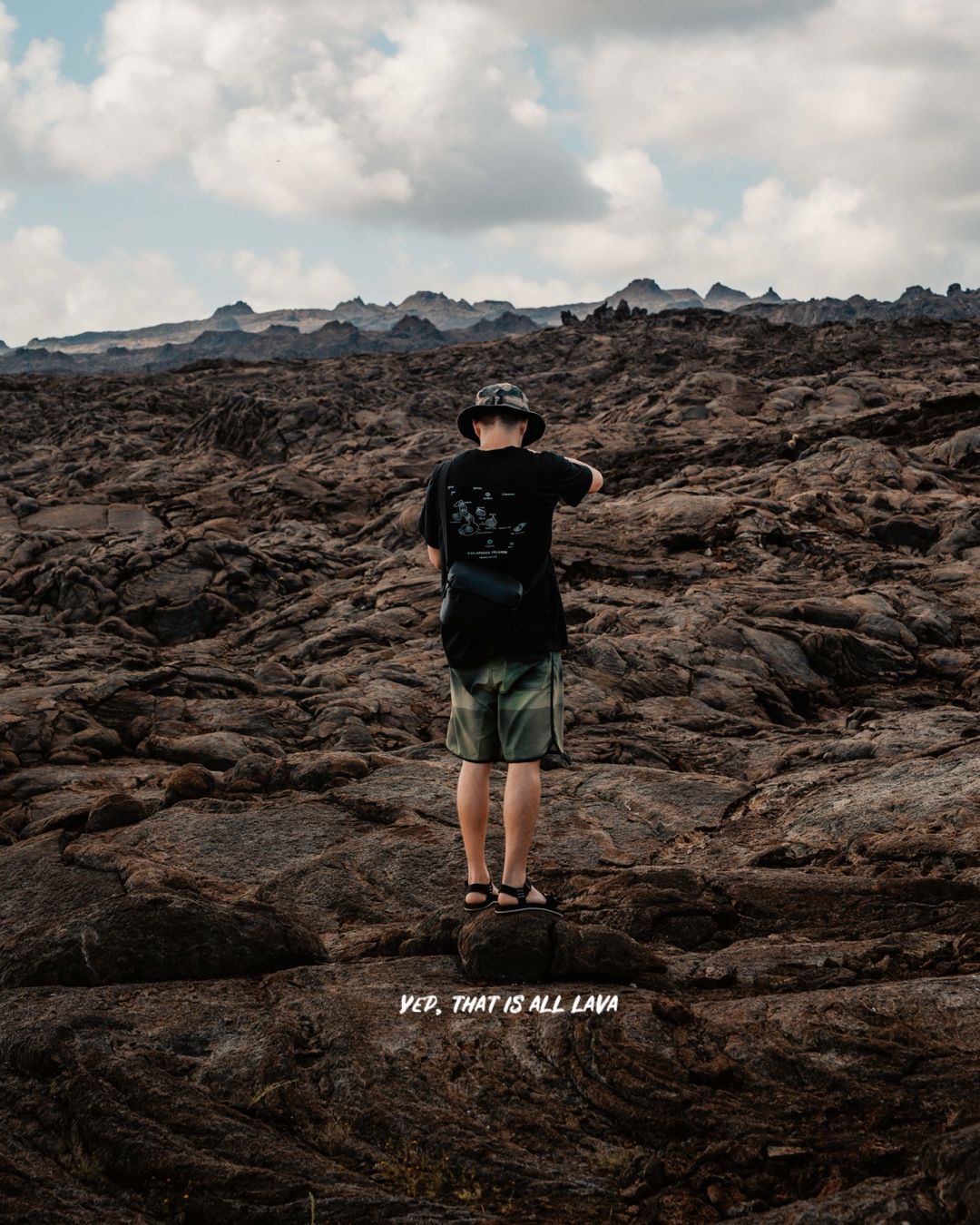 Figure standing on dark rocky volcanic terrain against moody cloudy sky.