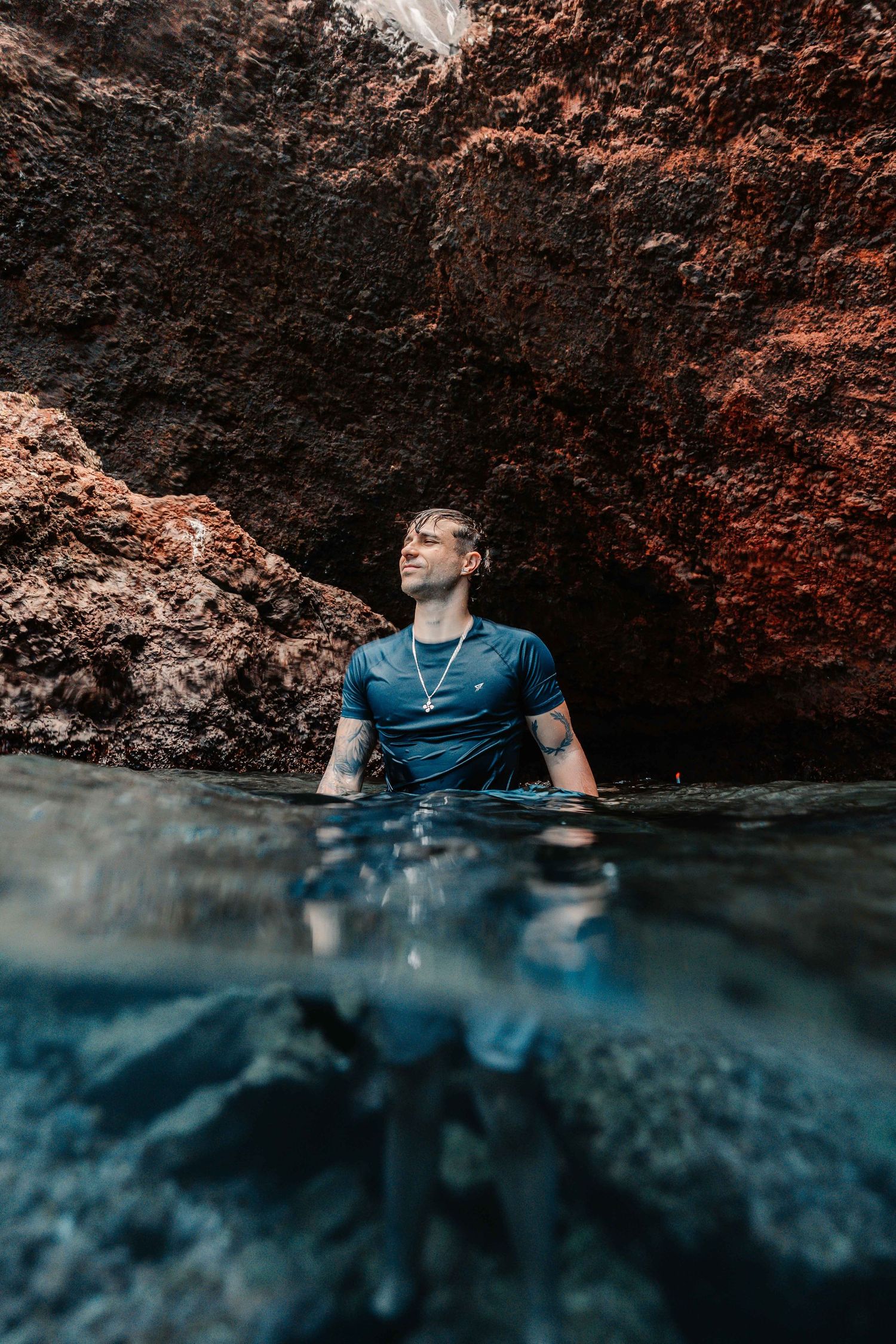 Split underwater shot showing swimmer resting against red rock wall.