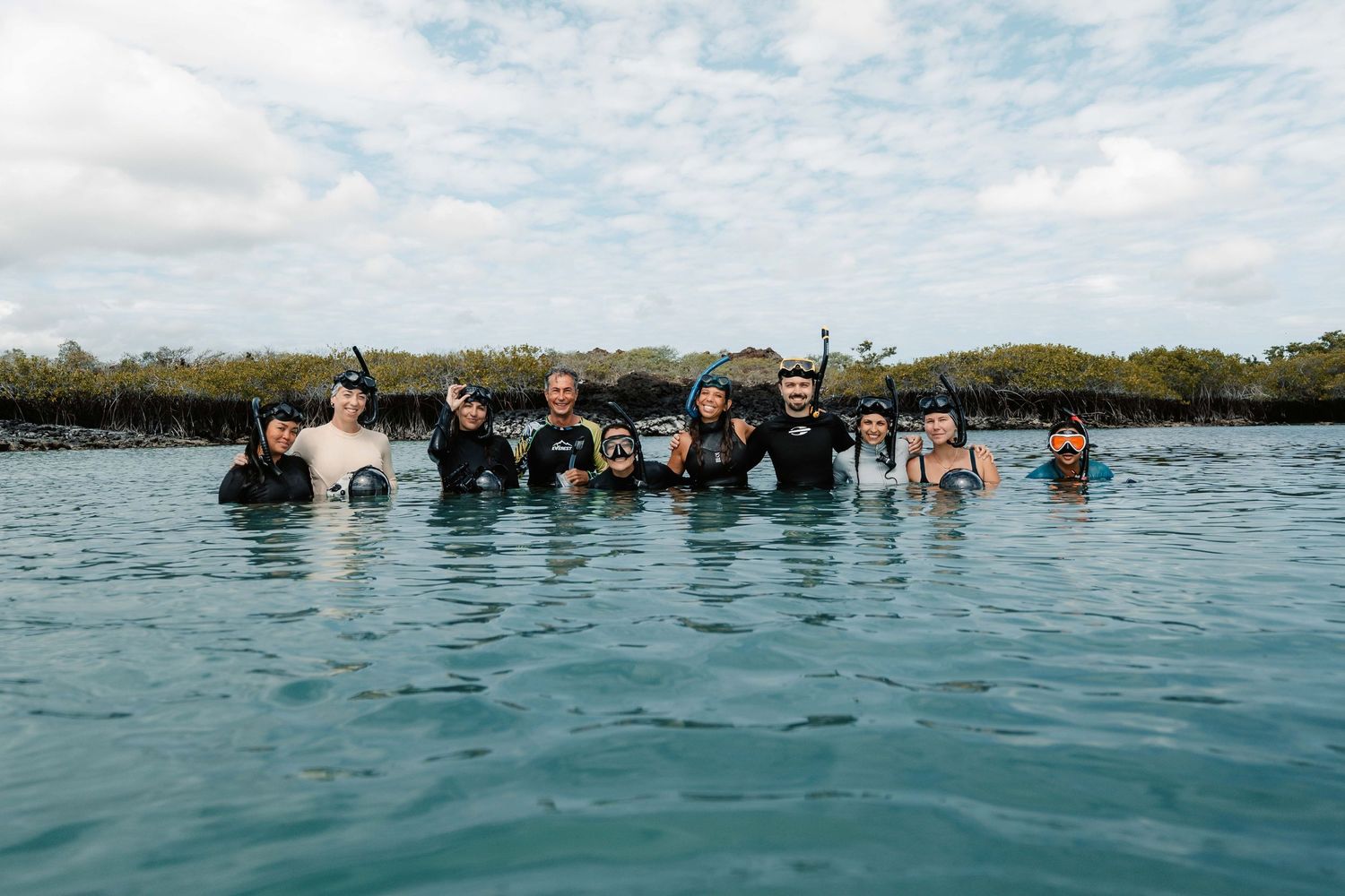 Group of snorkelers floating in clear tropical waters near mangroves on a sunny day.