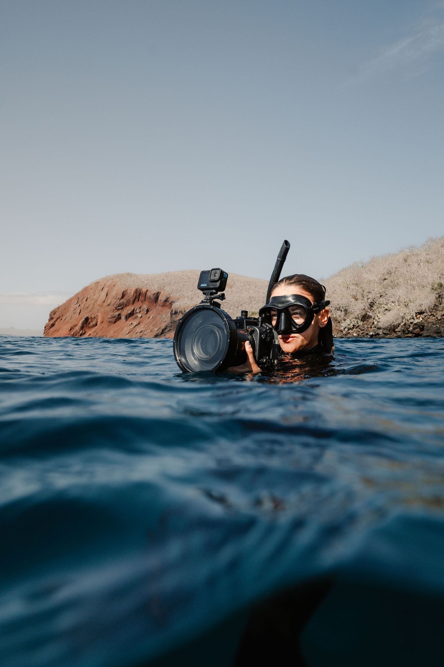 Underwater photographer with camera equipment floating at ocean surface.