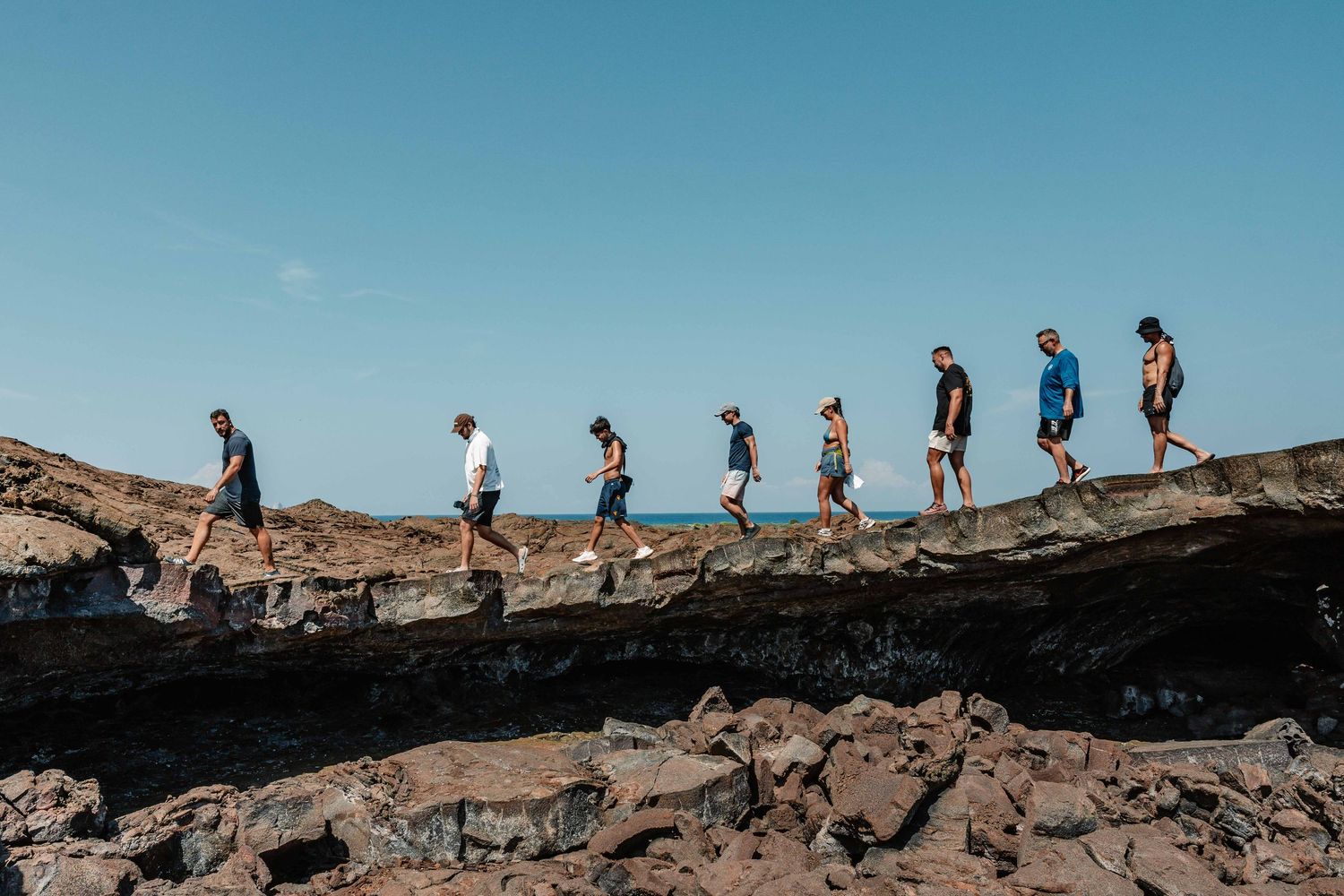 Group of hikers walking along rocky coastal cliffs with blue sky and ocean views.