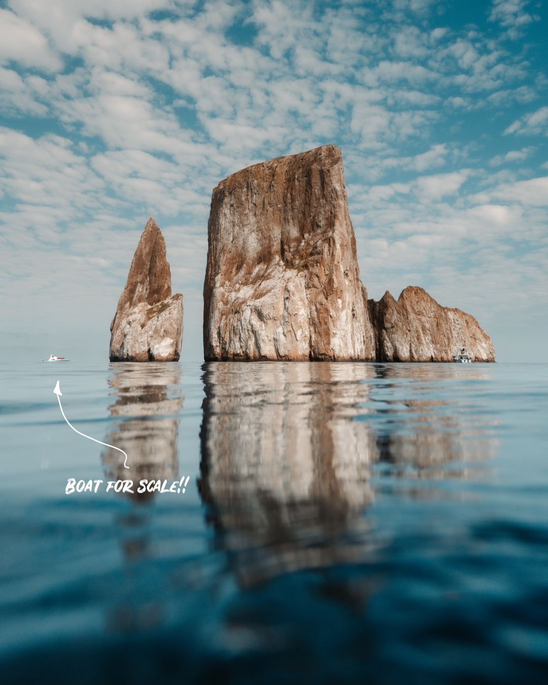 Dramatic rock formations rising from calm ocean waters under cloudy sky.