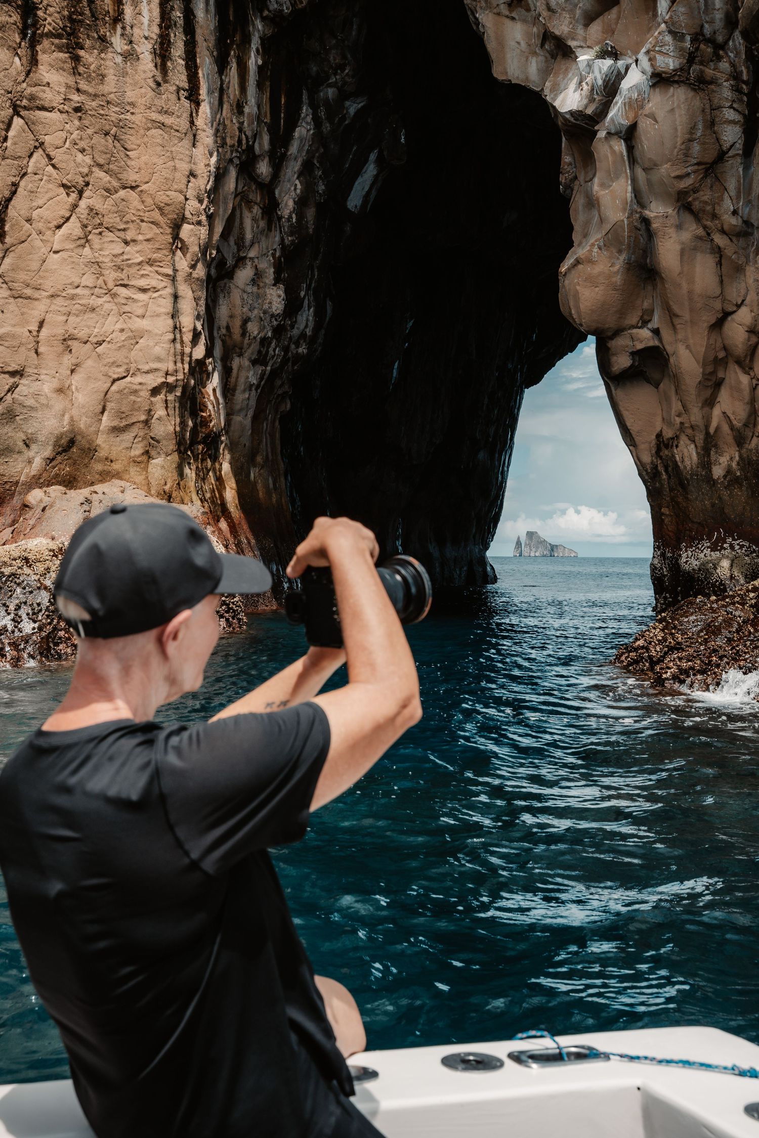 Photographer on a boat captures a stunning sea cave arch with a rocky island visible through the opening in blue waters.