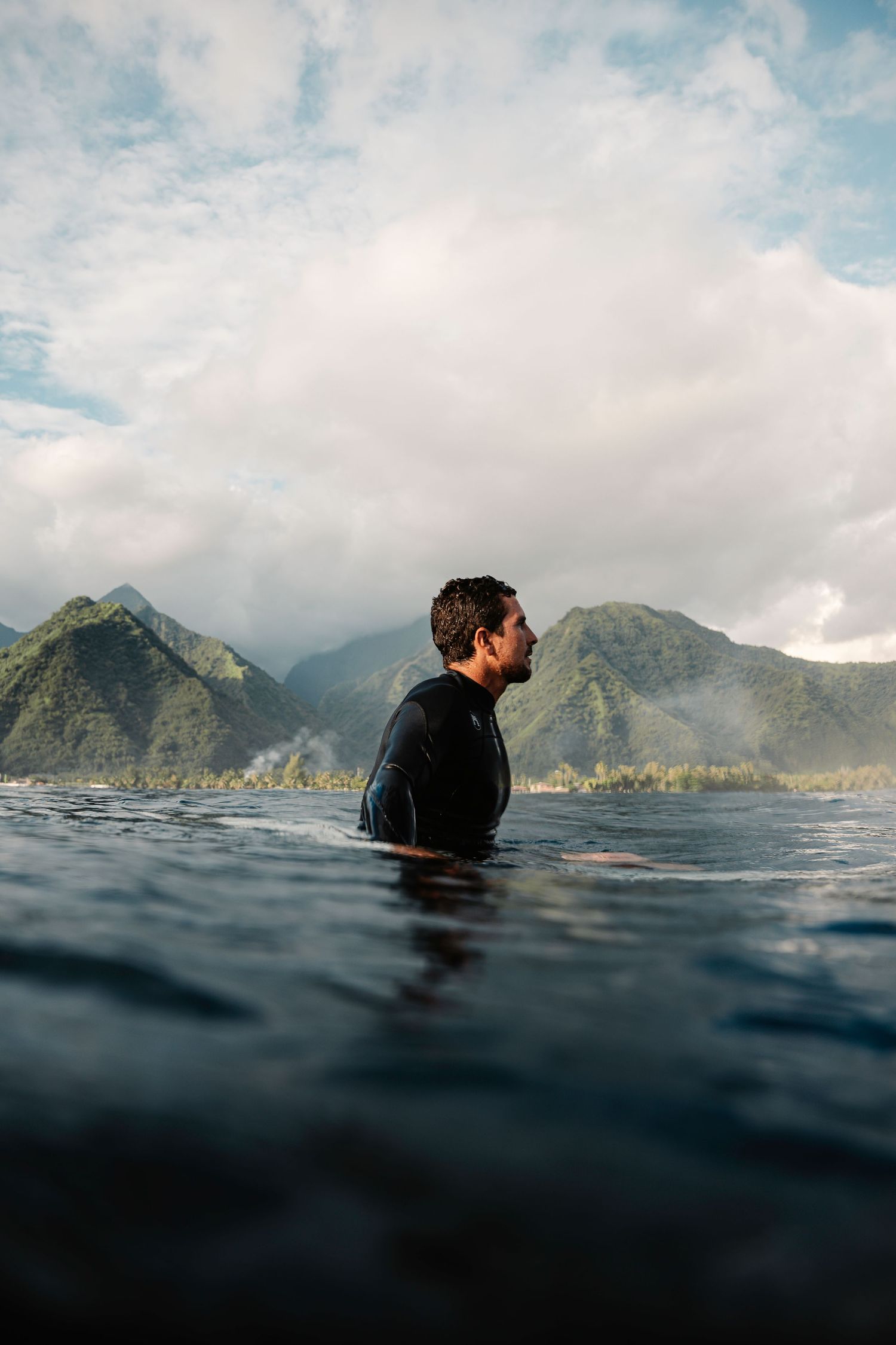 Sequence of a surfer in dark wetsuit floating in ocean water with dramatic mountain coastline and cloudy sky in background.