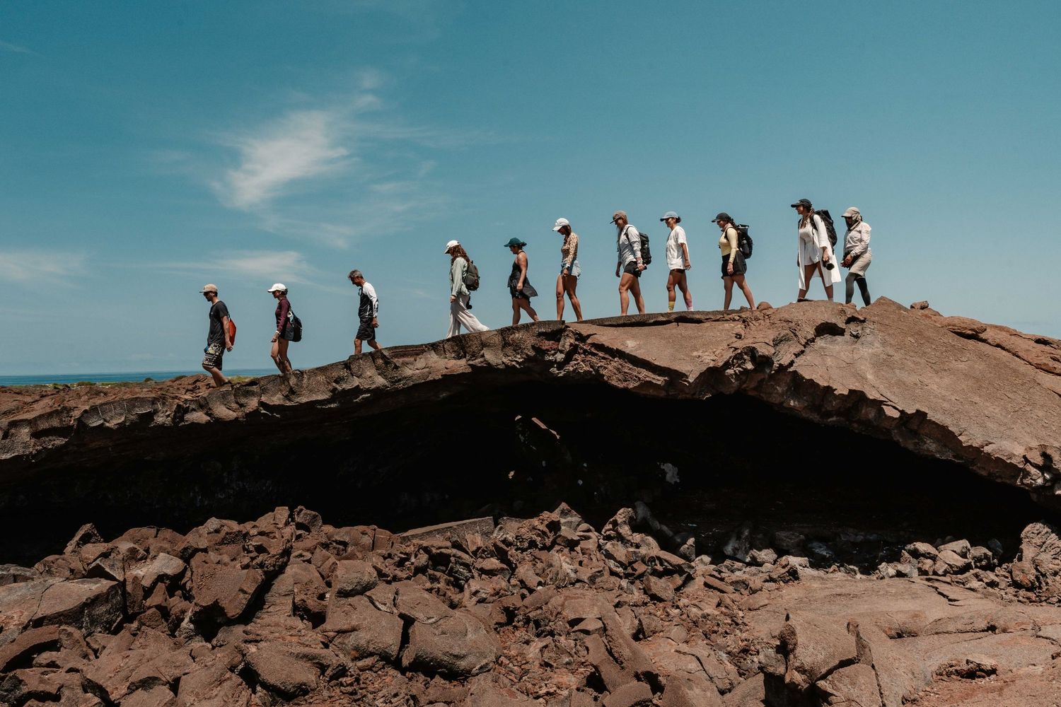 A line of hikers walking along the ridge of a sandy desert dune against a bright blue sky.
