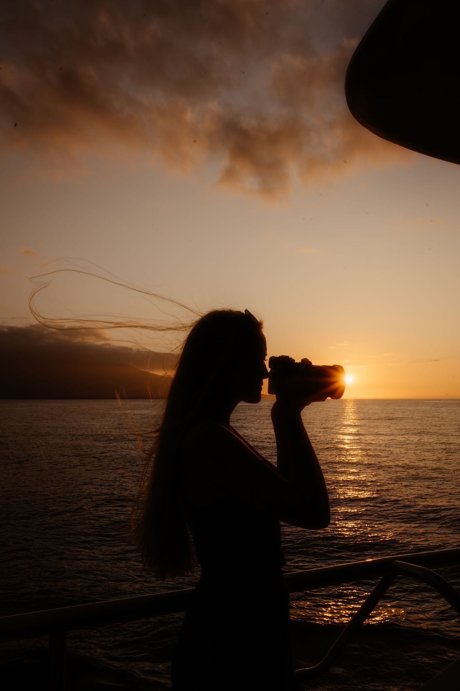 Silhouettes of a photographer against a dramatic orange sunset over the ocean.