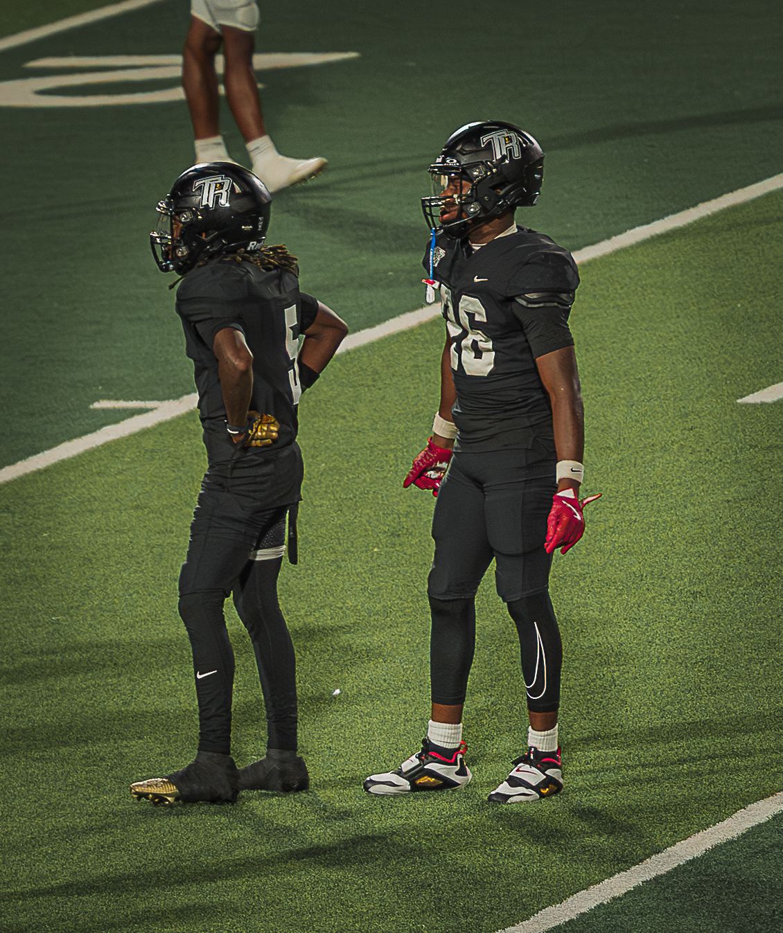 Football players in dark uniforms stand on the field during a game break.