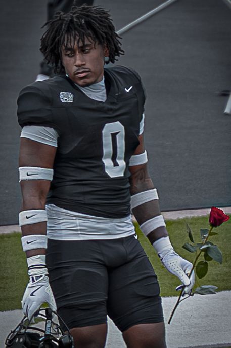 Football players in dark uniforms sit on the sidelines during a game break.