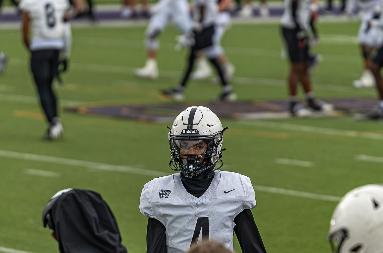 Football players in white and dark uniforms compete on a grass field during a game.