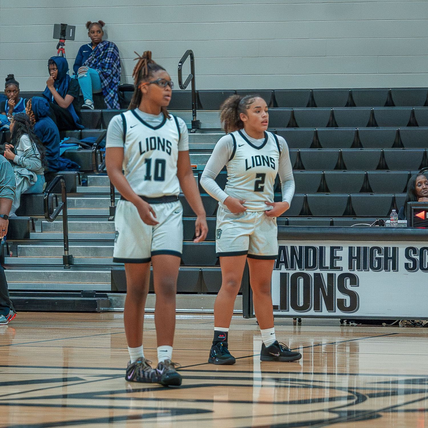 High school volleyball players in white Lions jerseys stand on the court during a match in a gymnasium.