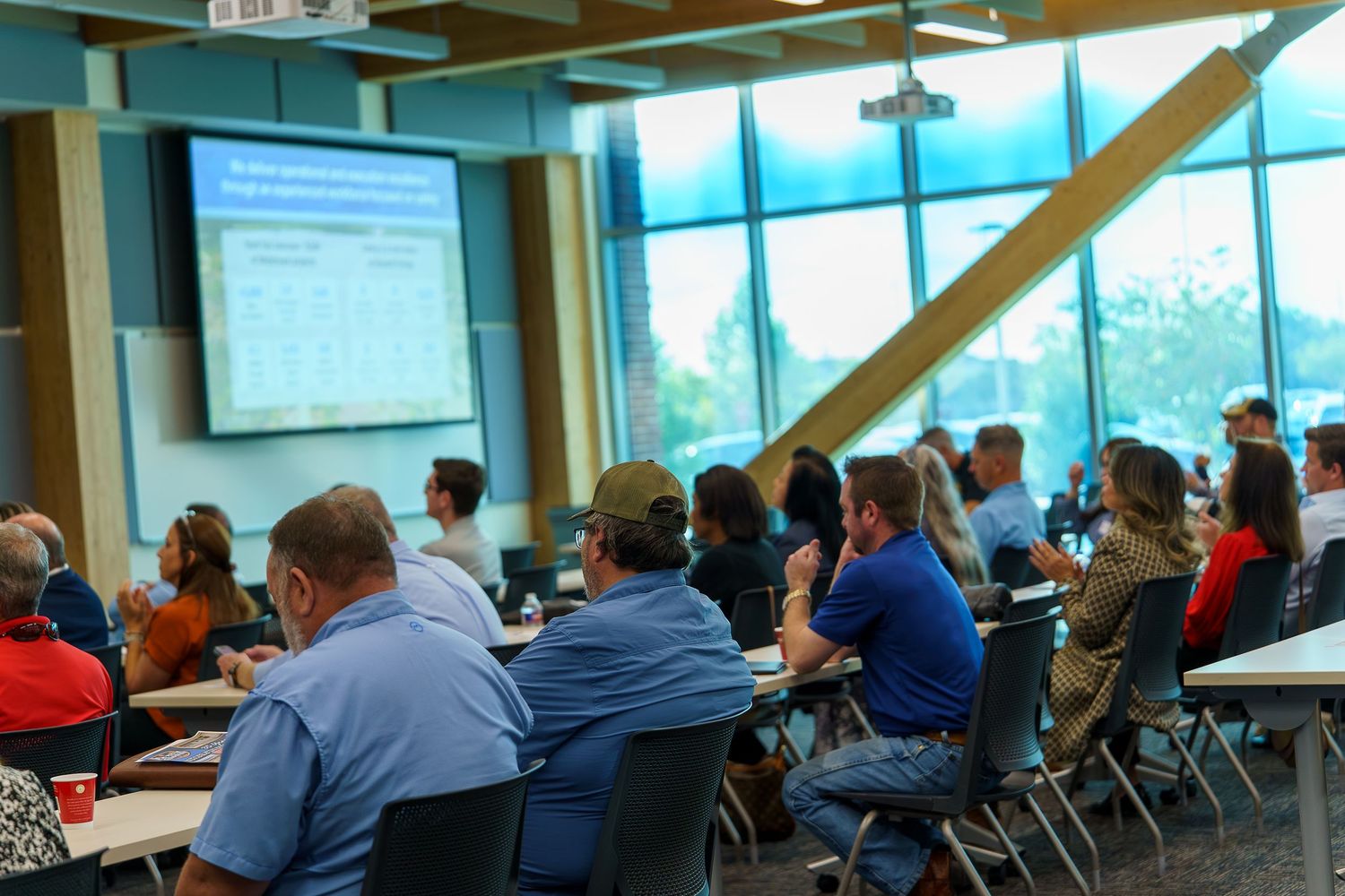 Conference room with large windows and audience members viewing a presentation.