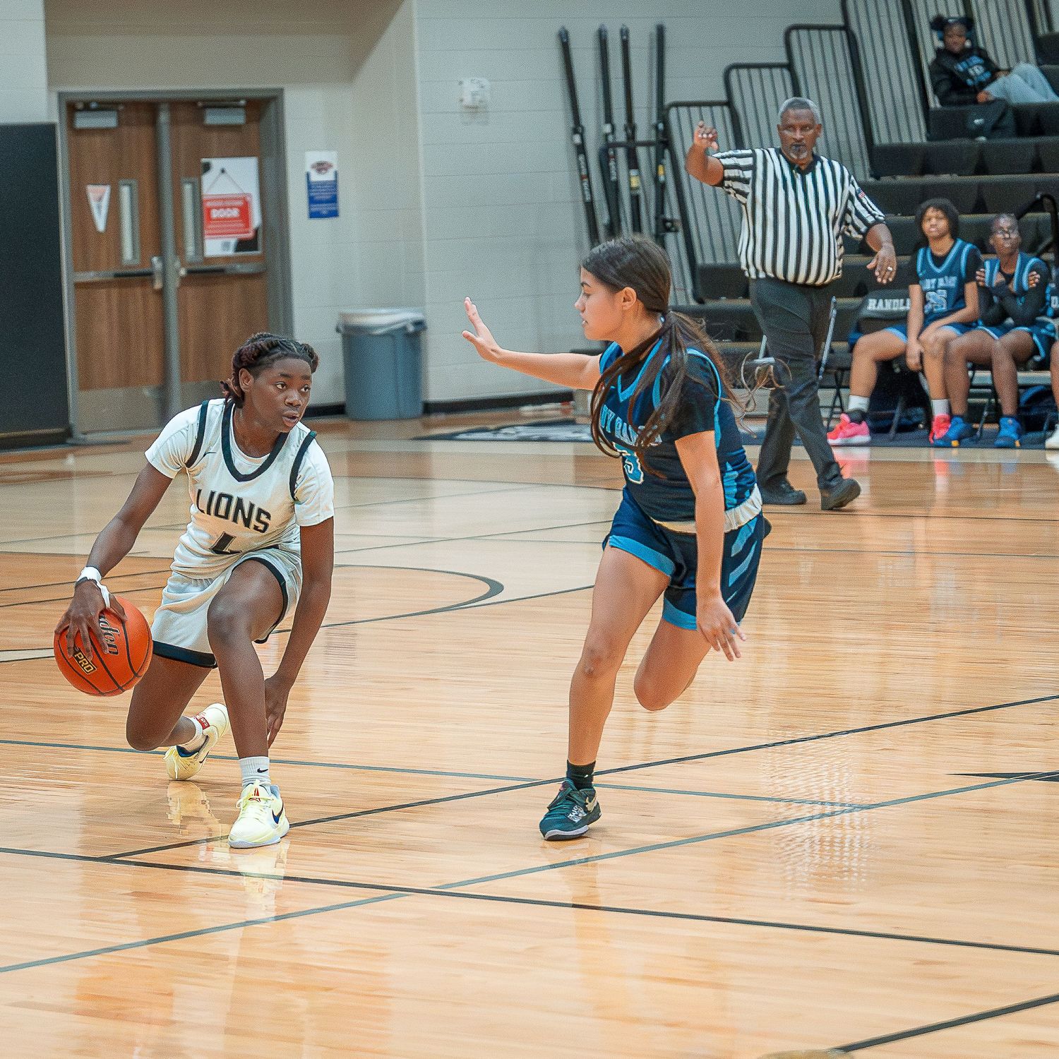 Basketball players in blue and white uniforms compete in an intense defensive drill on a gymnasium court.