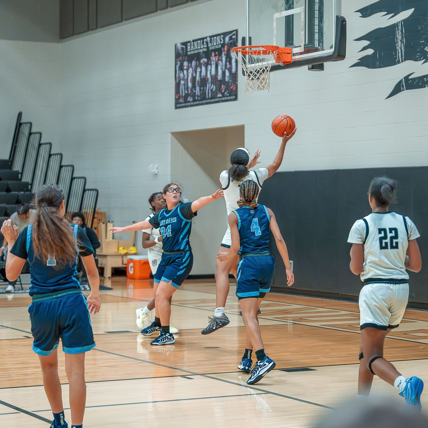 Basketball players in blue and white uniforms practice drills and shooting on an indoor court during a training session.
