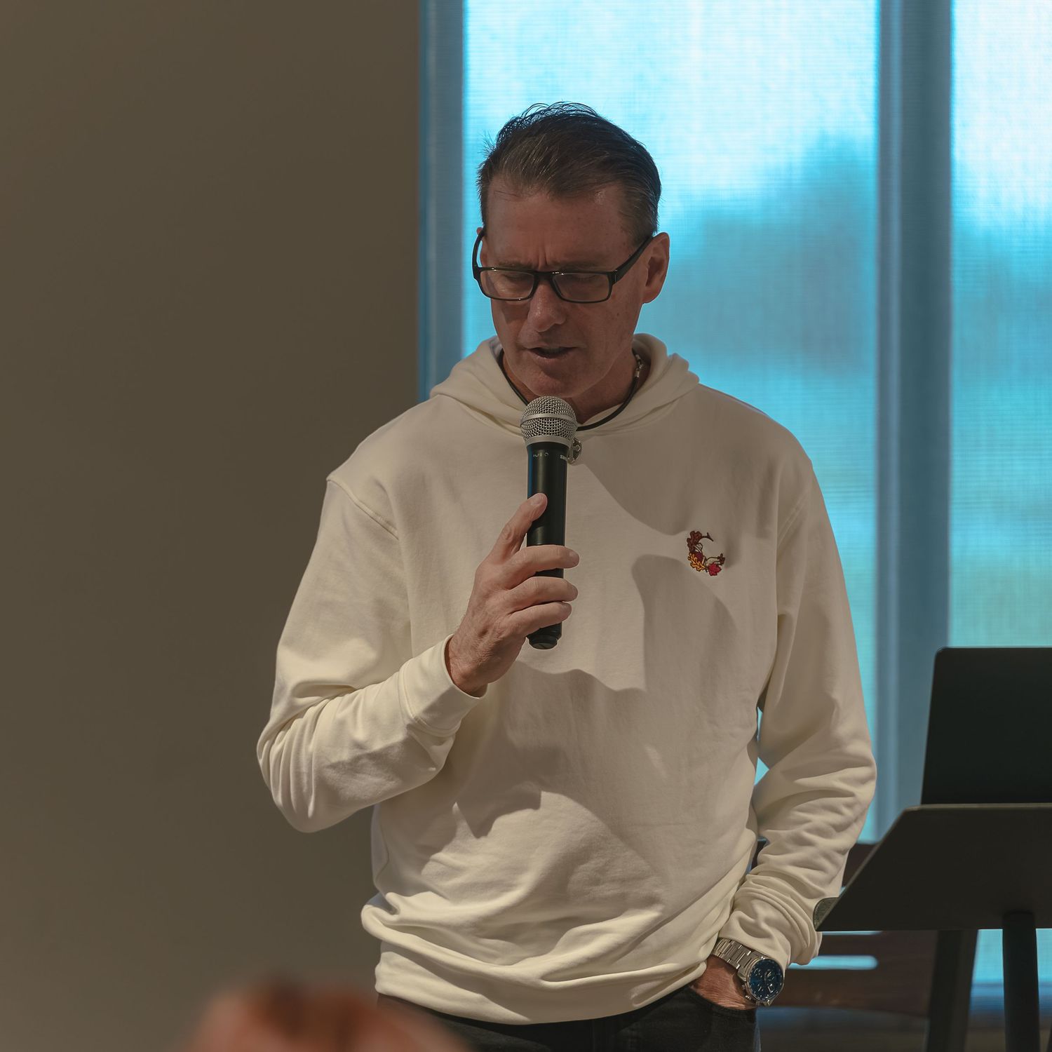 Person in white sweatshirt speaking into microphone during presentation.
