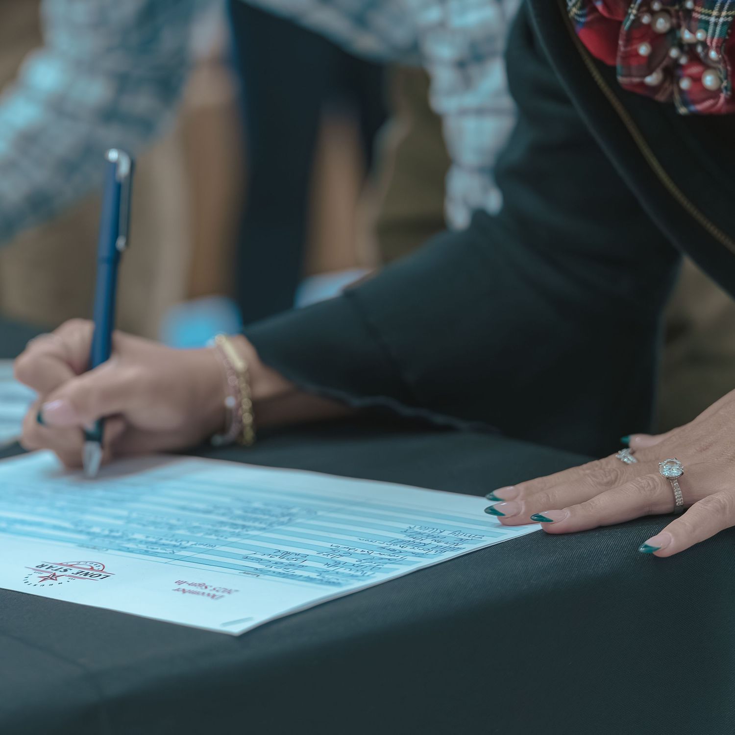 Close-up of hands signing documents on a dark surface.