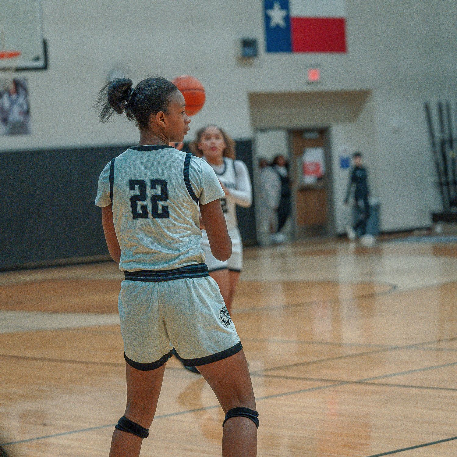 Basketball player wearing jersey number 22 stands on indoor court with Texas state flag visible in background.