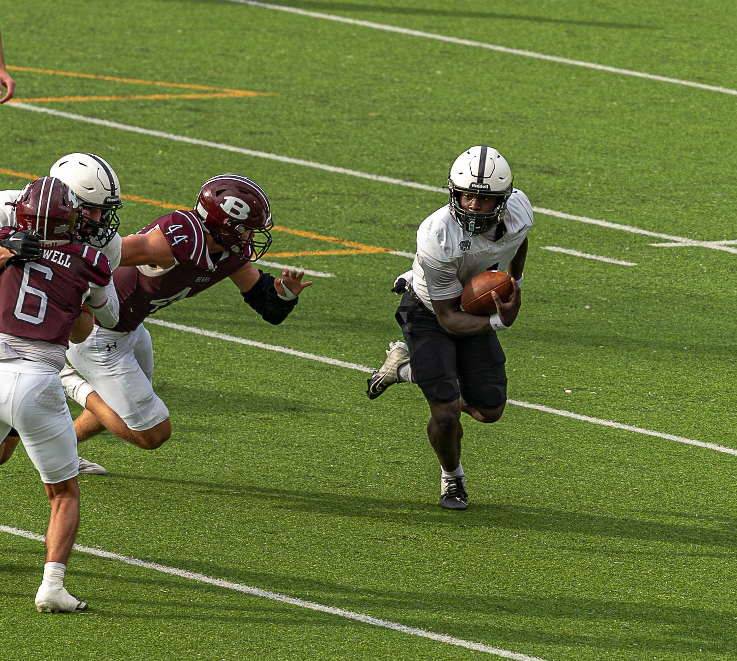 A football player dives forward while carrying the ball during an intense game on a green turf field.