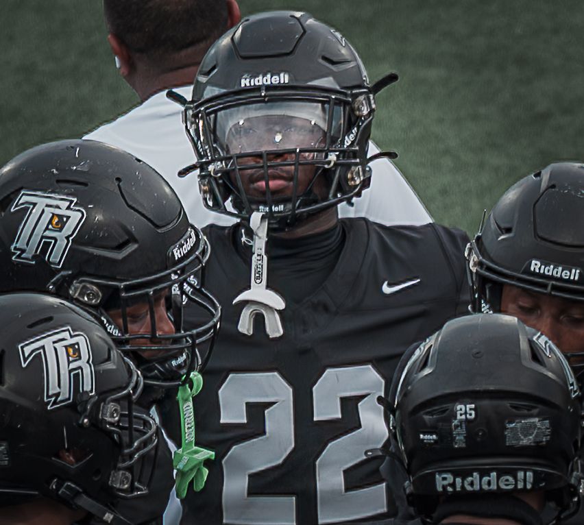 Football players in black uniforms and helmets huddled together on the field.