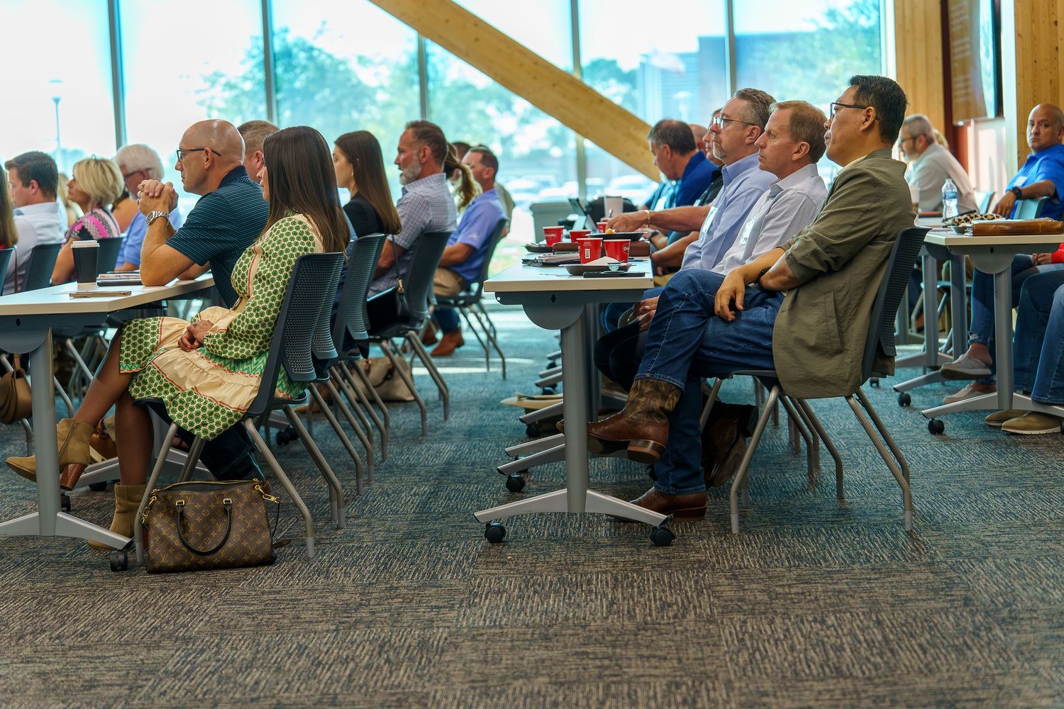 Business professionals seated in rows at tables during a corporate conference or meeting in a modern venue.
