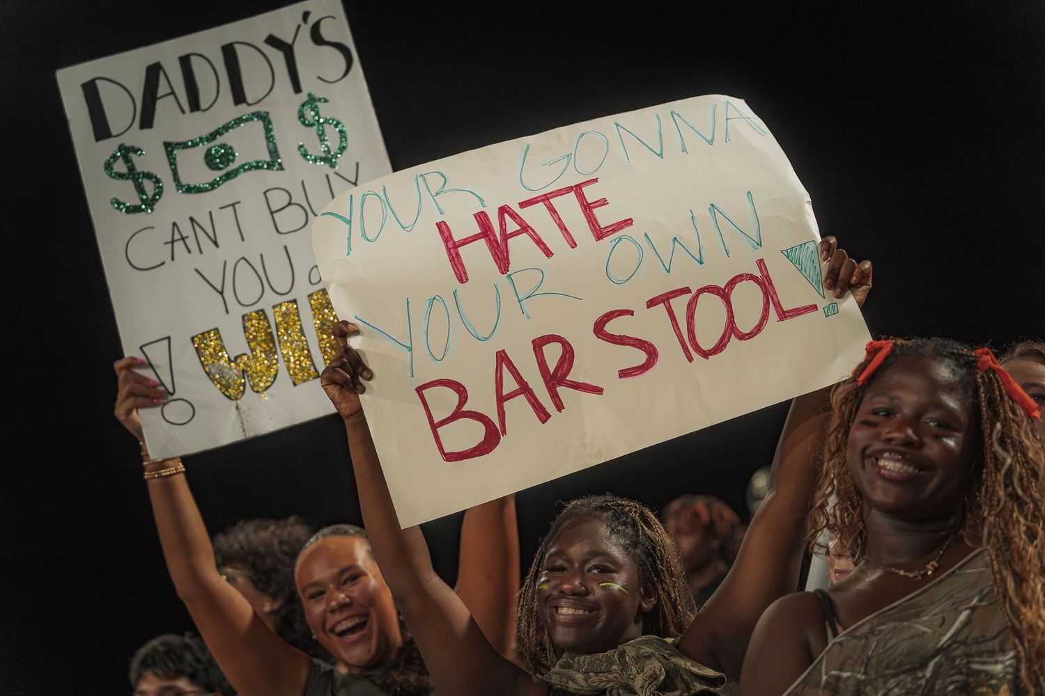 Protestors hold up signs expressing opposition to Barstool Sports at a nighttime demonstration.
