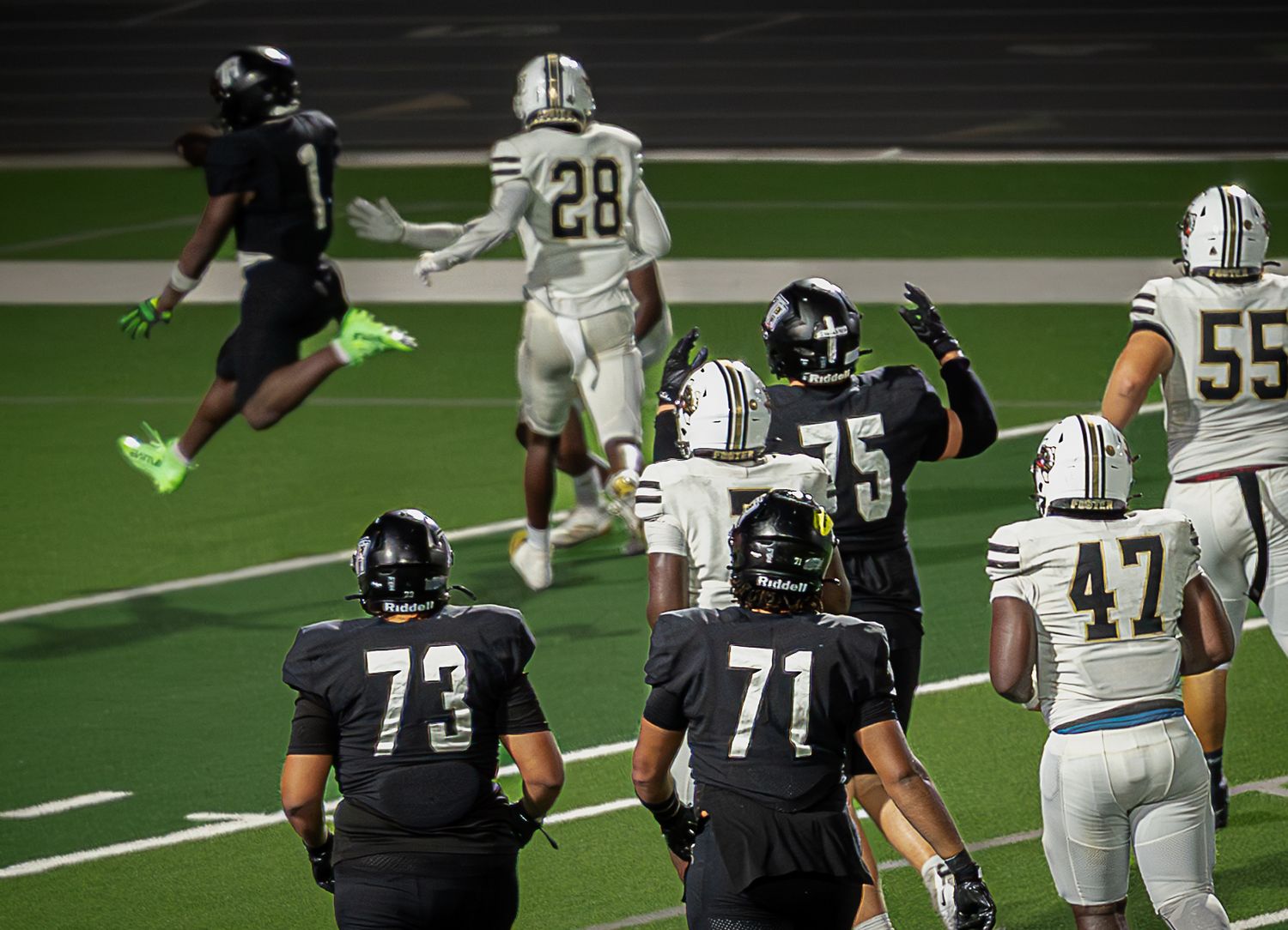 Football players in black and white jerseys line up for a play during a night game.