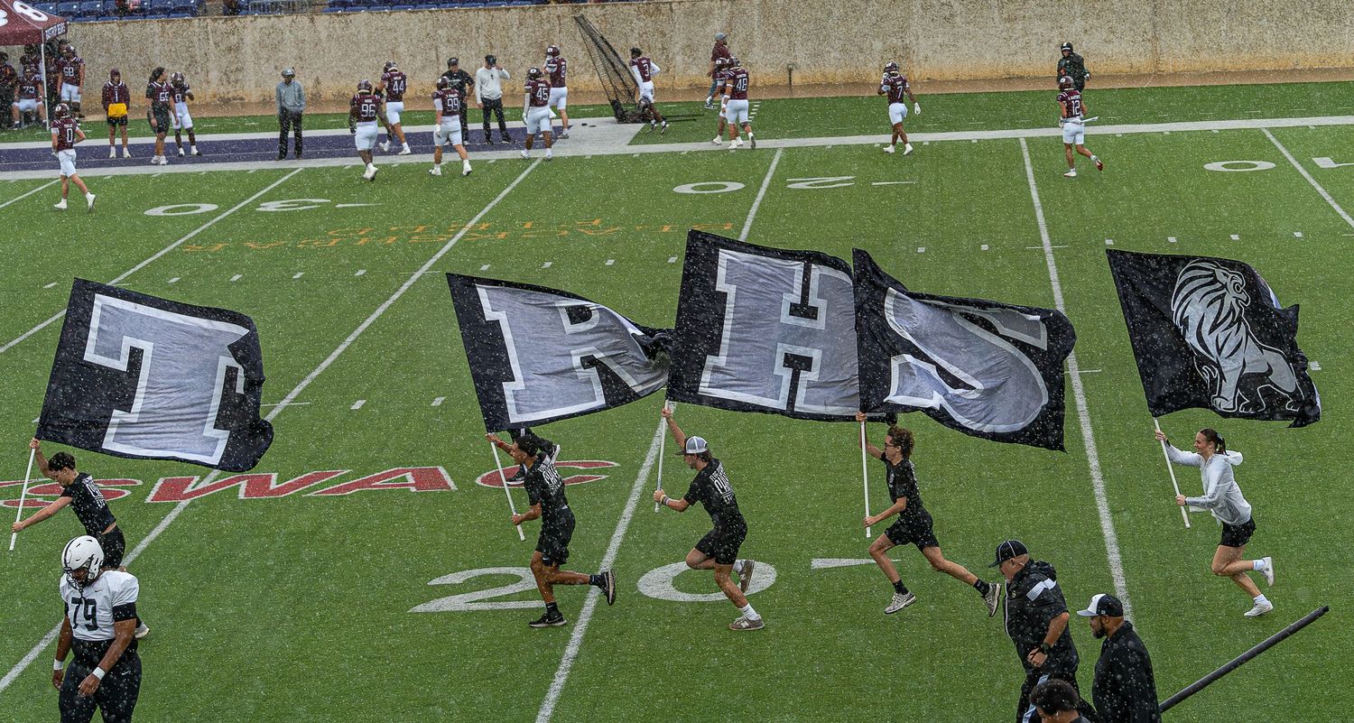 Players compete in an outdoor football game on a green turf field with yard lines and markings visible.