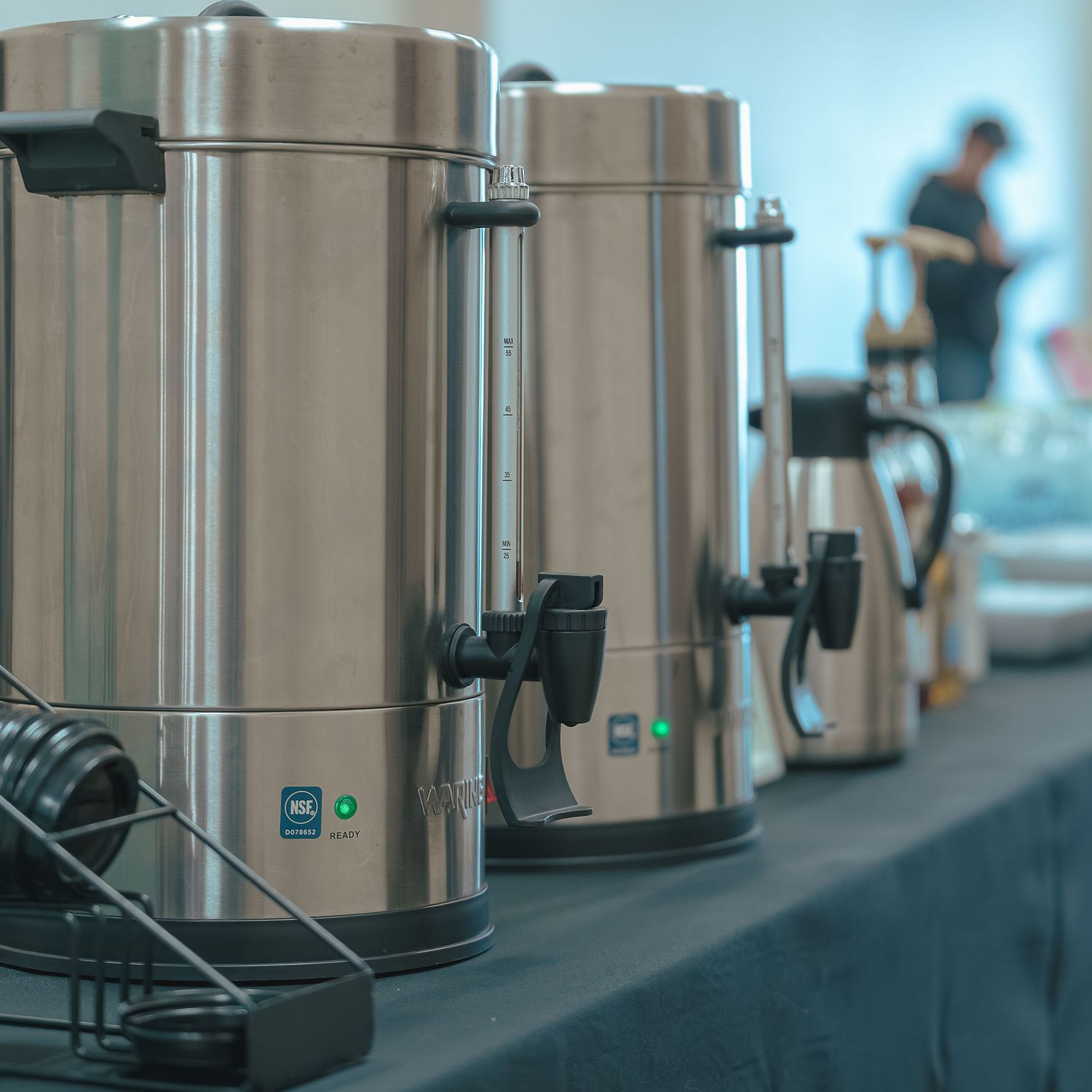 Row of silver coffee dispensers lined up on a dark counter.