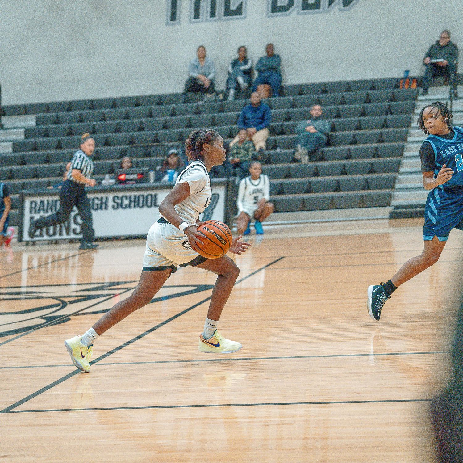 Basketball player performs a series of dribbling moves on a gym court with stadium seating in the background.