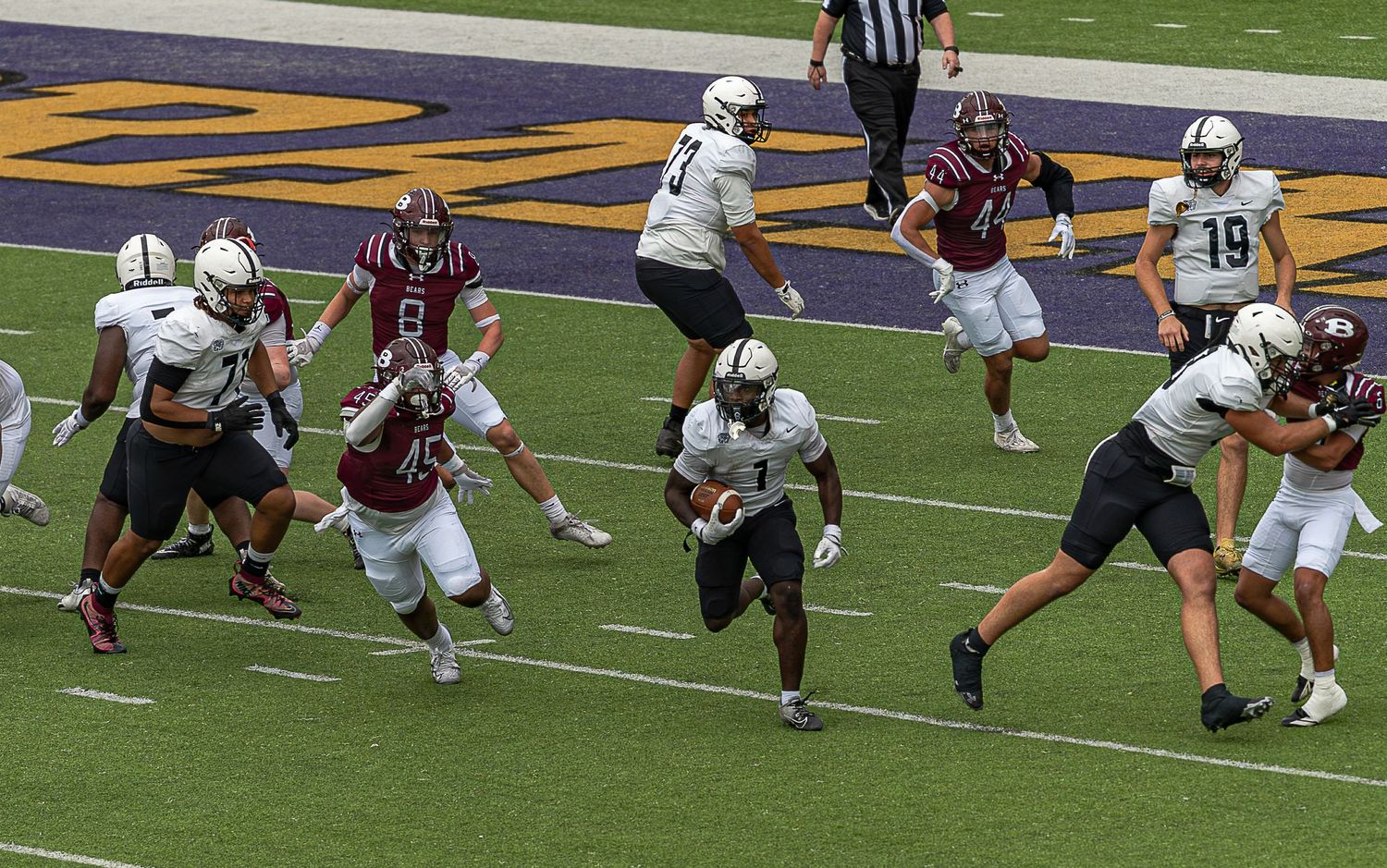 College football players compete during a game with offensive and defensive players engaged in live action on the field.