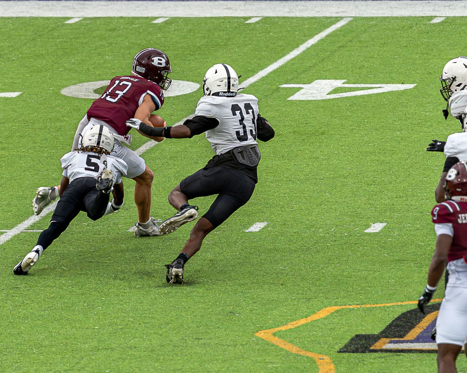 Football players compete during a game on a bright green turf field with yard line markings visible.