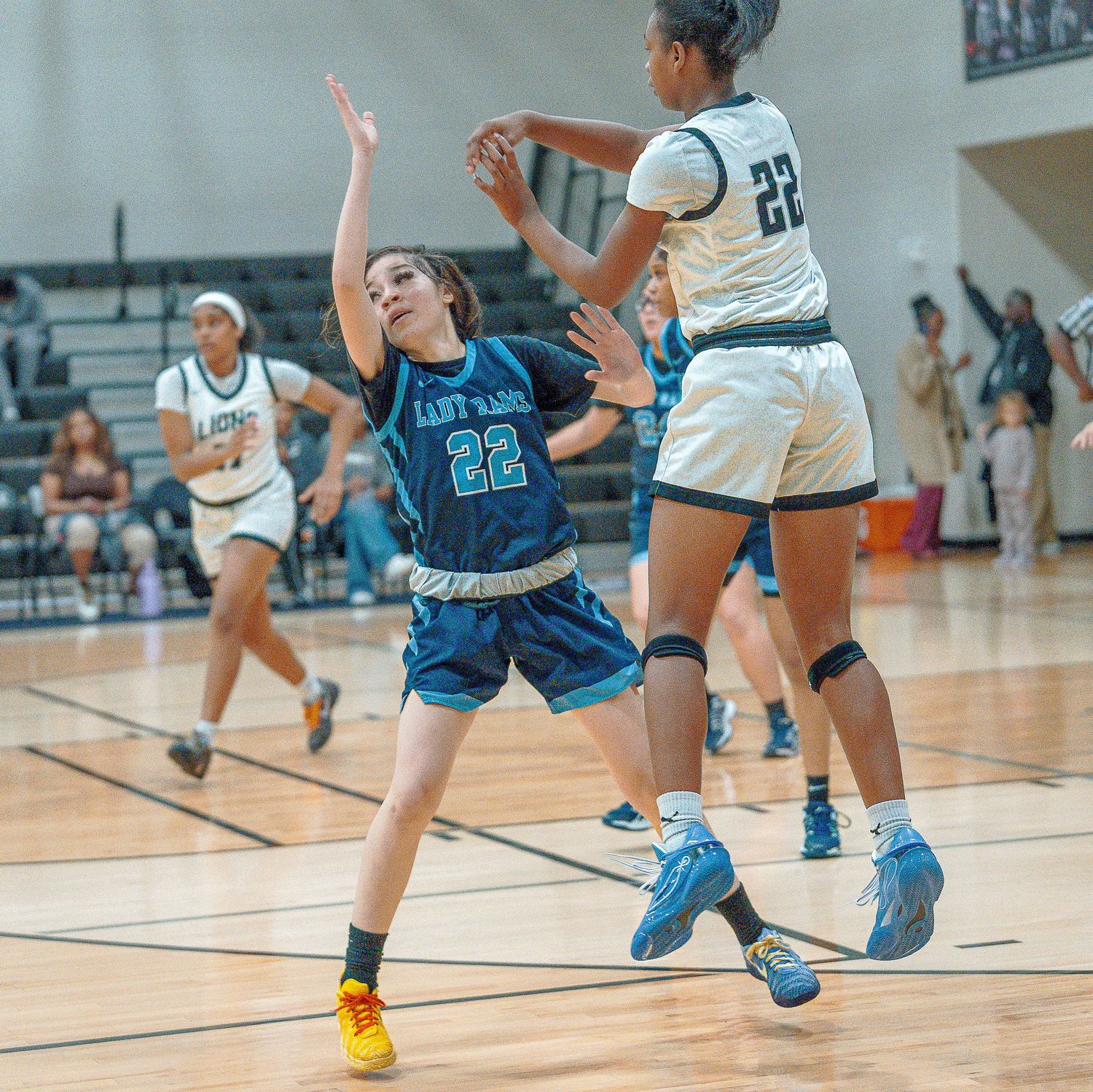 Basketball players compete for possession during an intense indoor game with one player in blue and another in white.