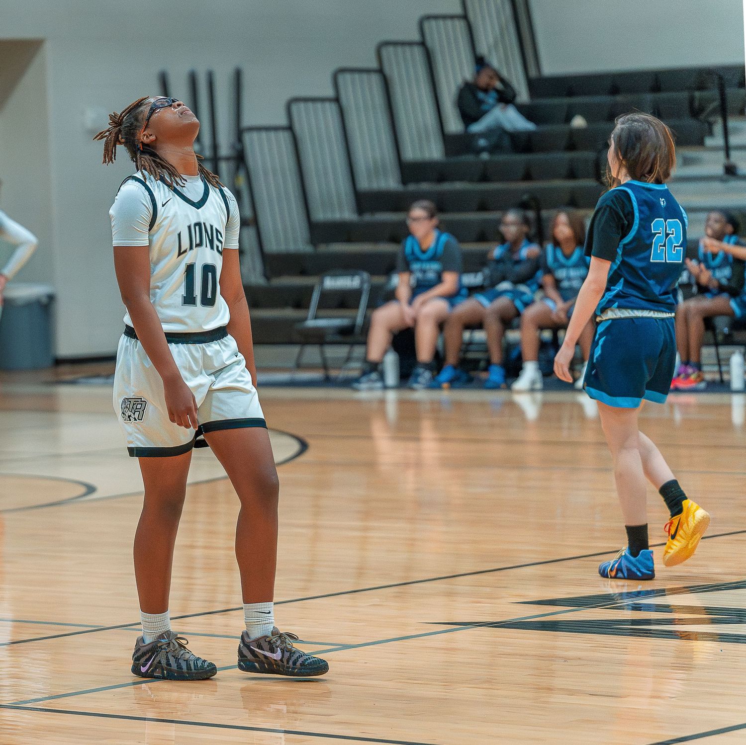 Basketball players from opposing teams in white and blue uniforms stand on court during competitive game action.