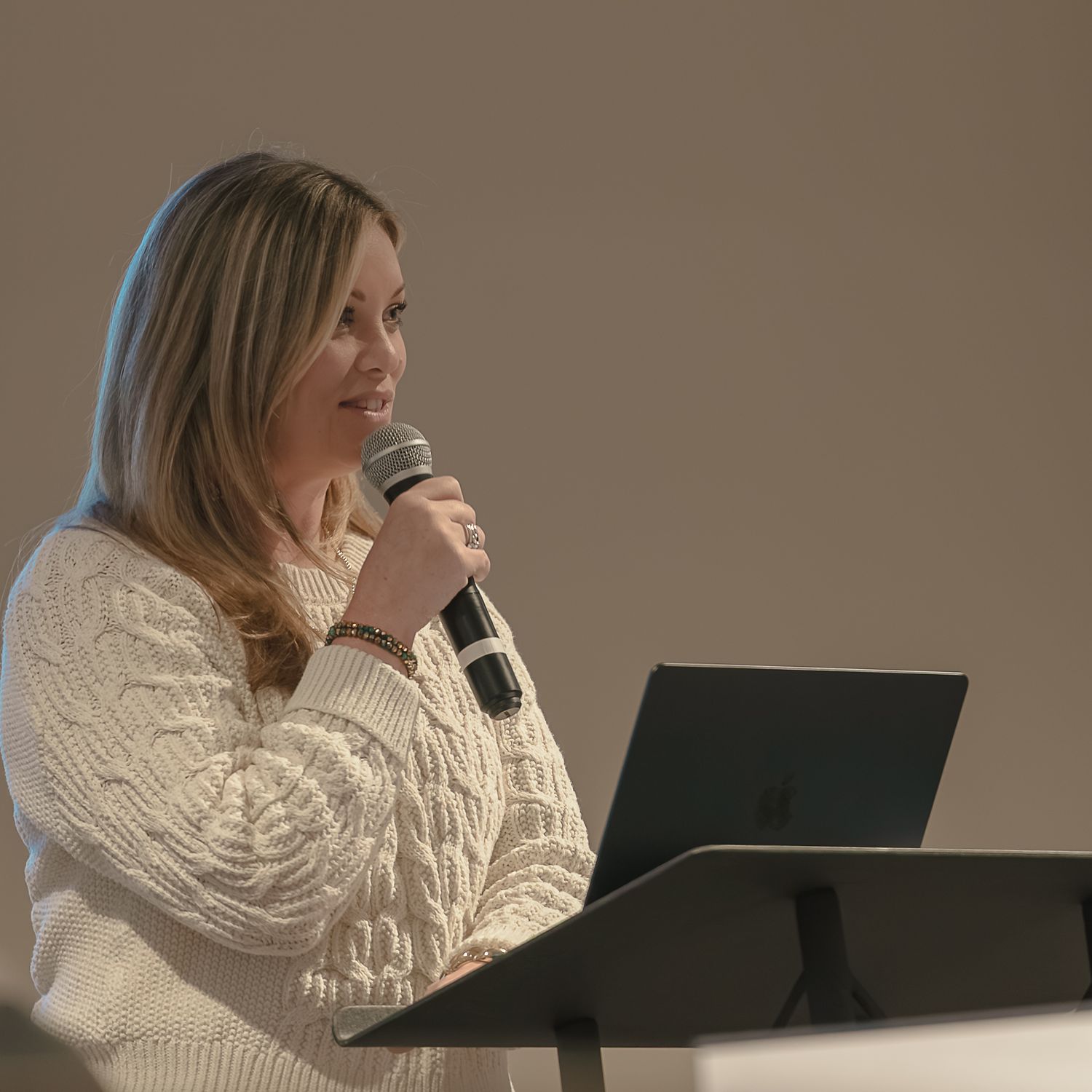 Speaker in white sweater presenting at podium with microphone.