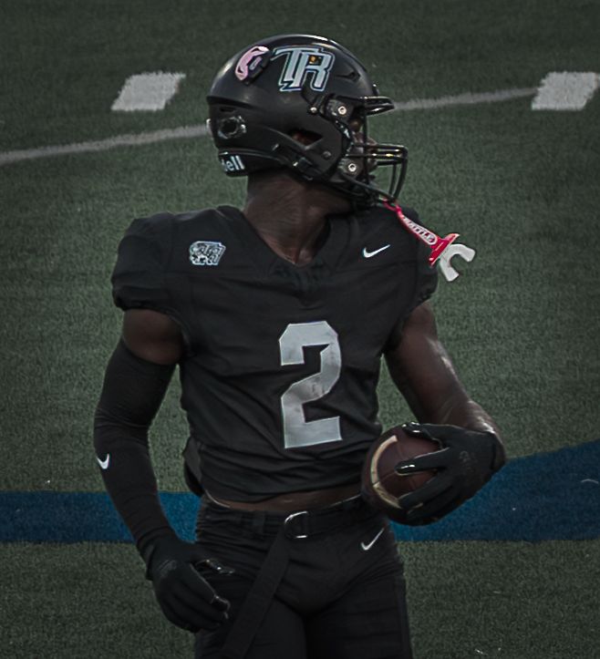 Football player wearing black jersey number 2 carries ball during gameplay.