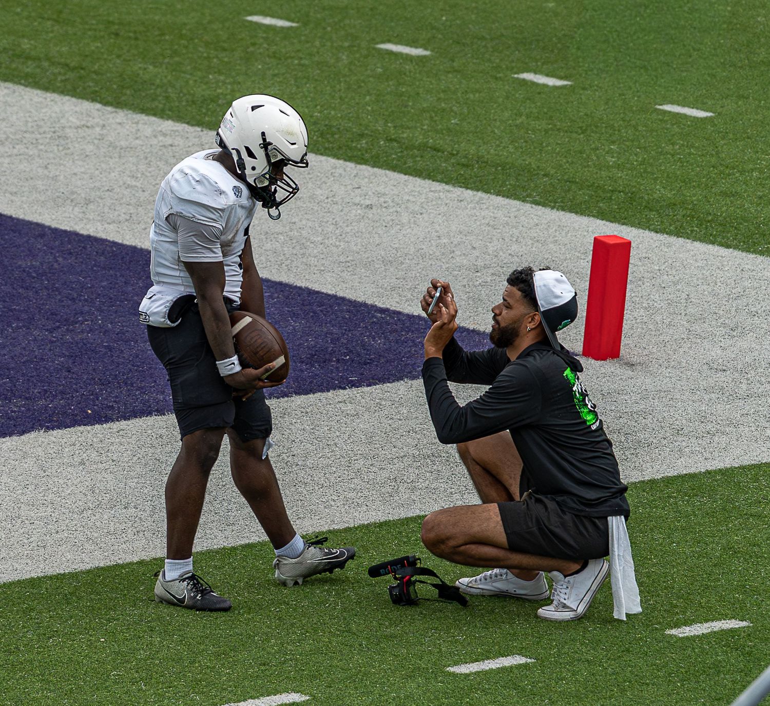 Athletes kneel on the sideline of a football field during a game.