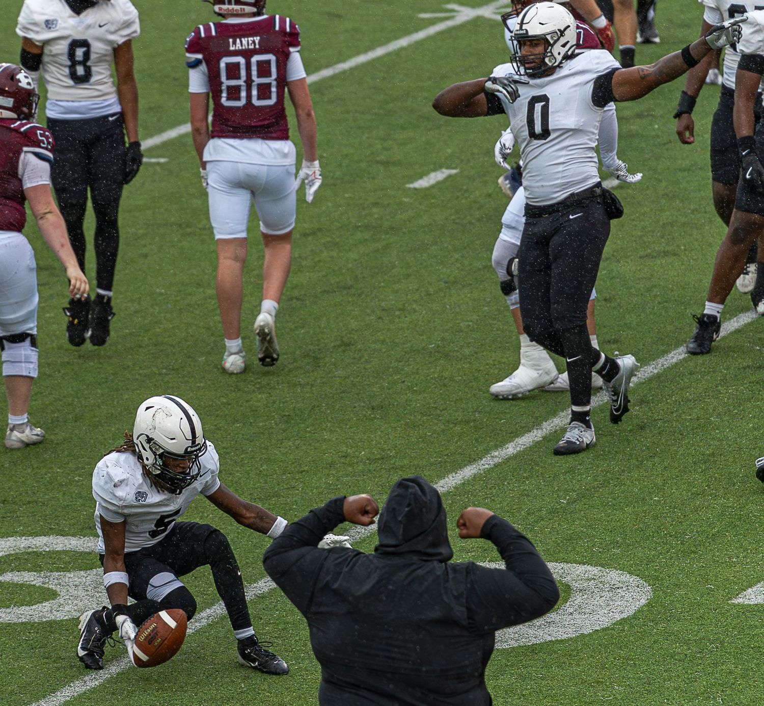 Football player in white uniform recovers a fumble on the field while a referee signals the play.