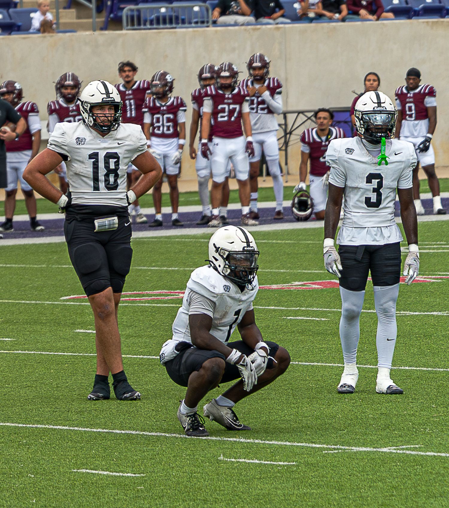 Football players from two teams on field during game with one player crouched down in center position.