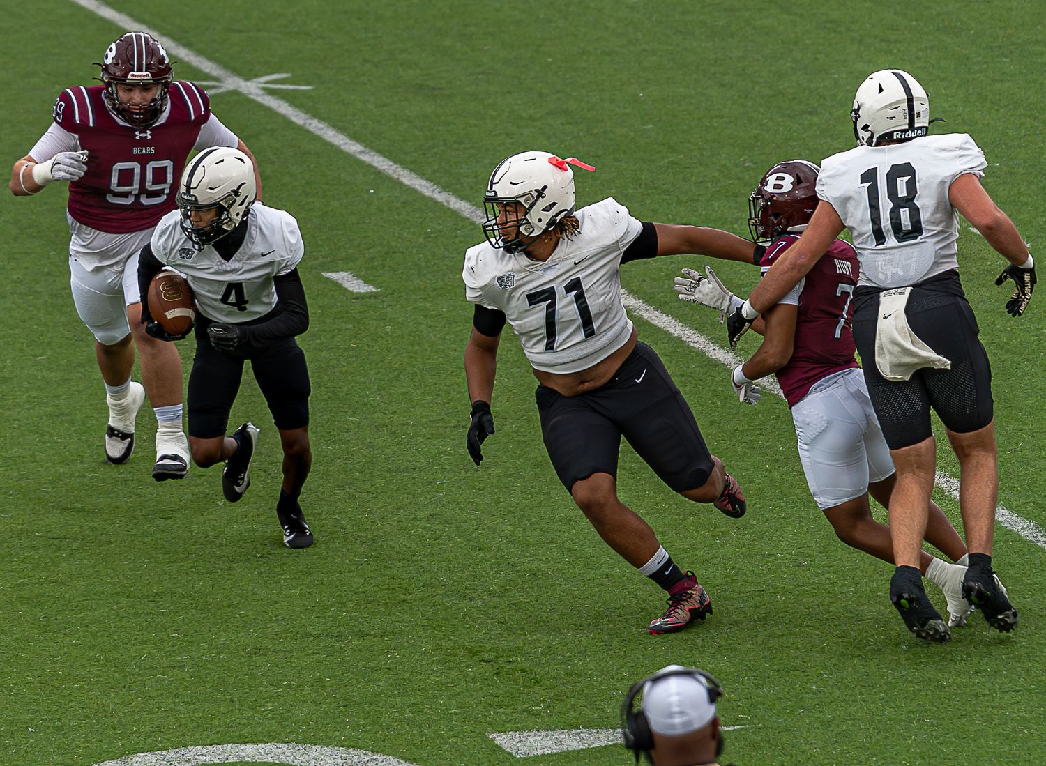 Football players in red and white uniforms engage in a blocking drill during practice on a grass field.