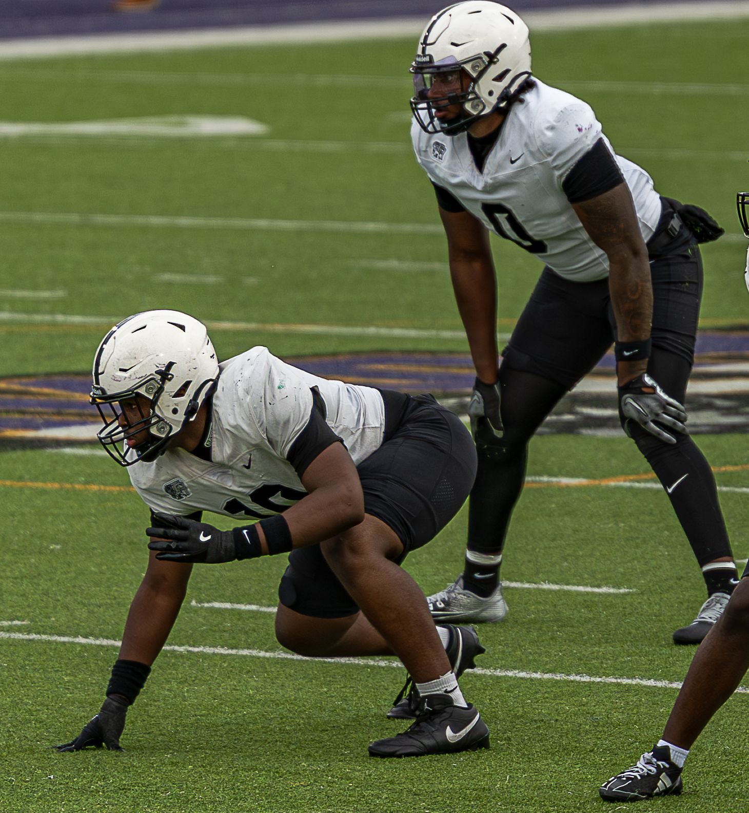 A sequence of football players in white uniforms crouching in defensive stance positions on a green turf field.