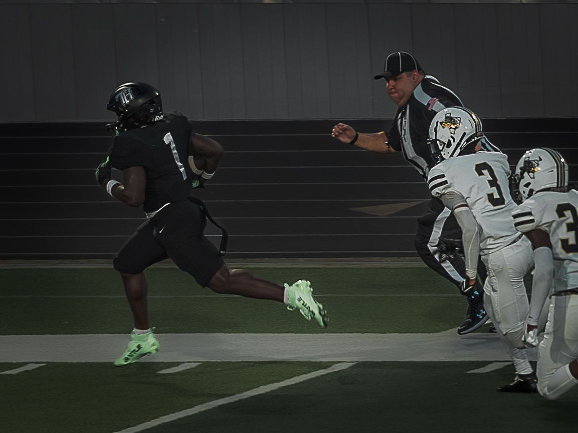 Players compete for position during a football play with one player leaping in the air.
