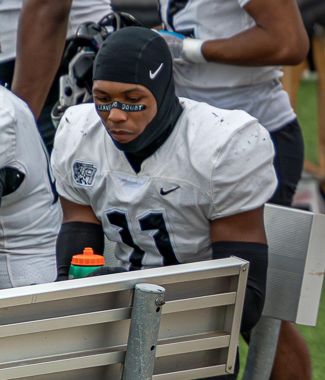 Football players lean against an aluminum bench during a game while wearing white uniforms and Nike gear.