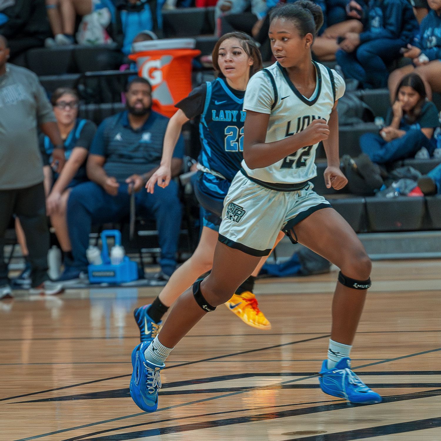 Basketball players in blue and white uniforms crouch in defensive positions during an intense game on the court.