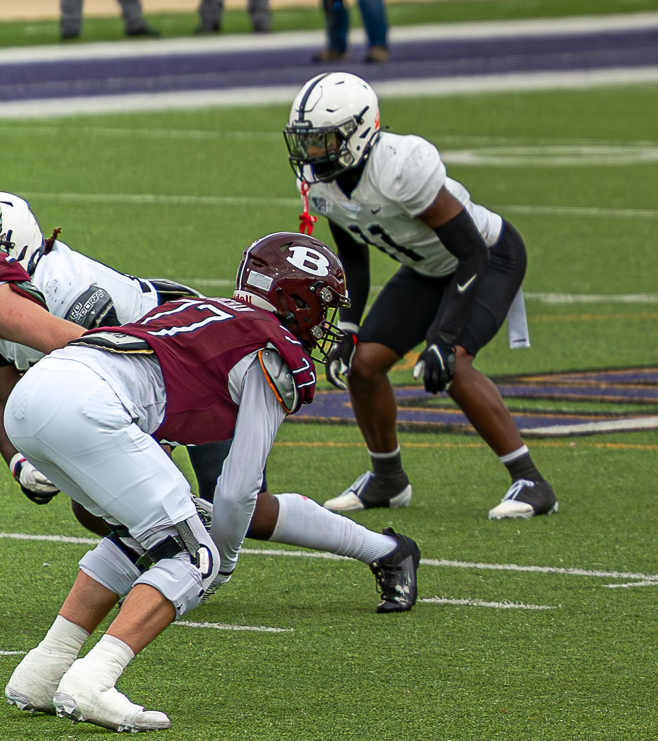 Football players in white and maroon uniforms dive and tackle during an intense game on the field.