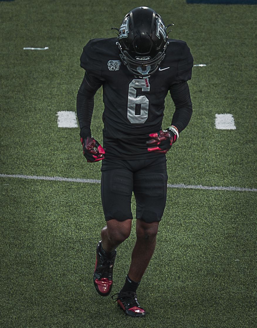 Football players in black uniforms with pink accents stand ready on the field.