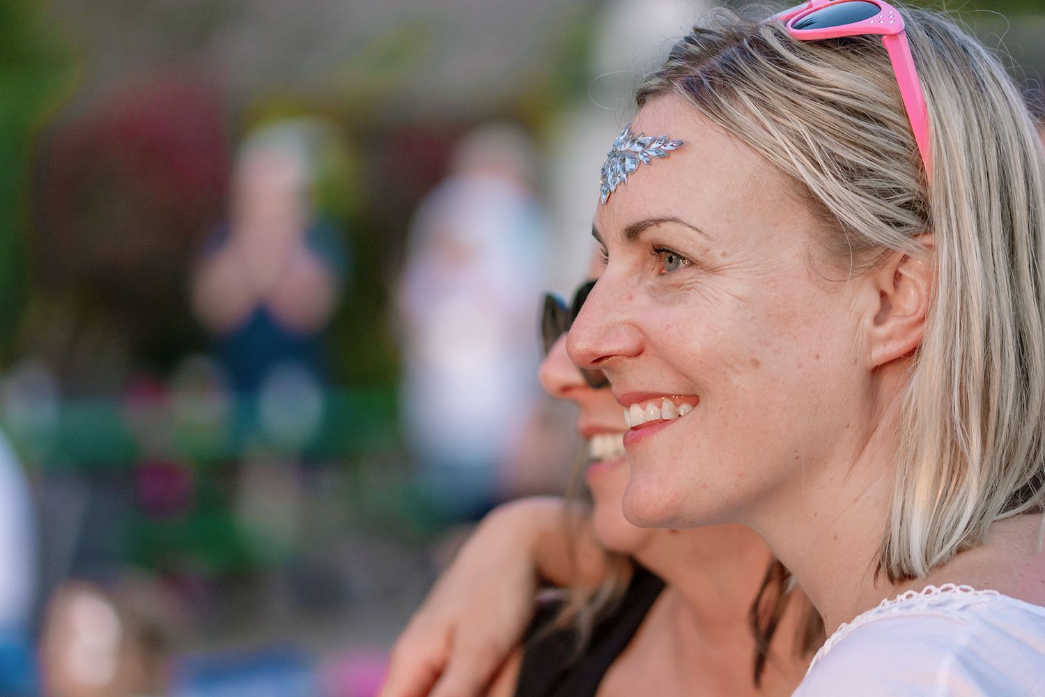 Side profile portrait of someone with blonde hair wearing sunglasses and smiling outdoors on a sunny day.