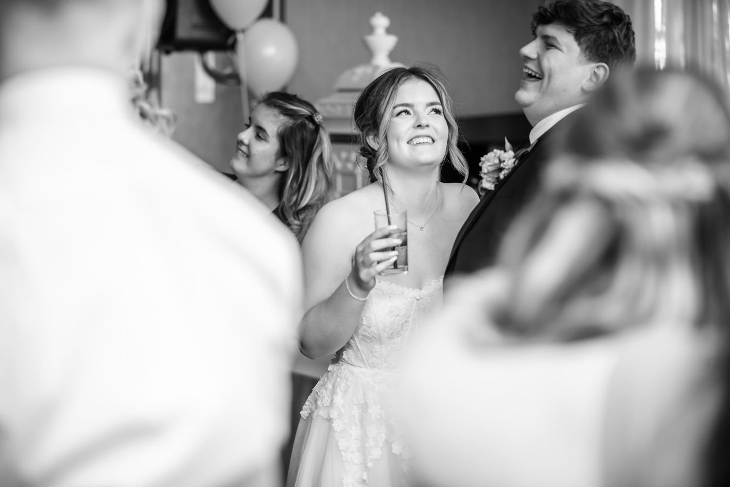 Black and white photo of a smiling bride holding a drink at her wedding reception.