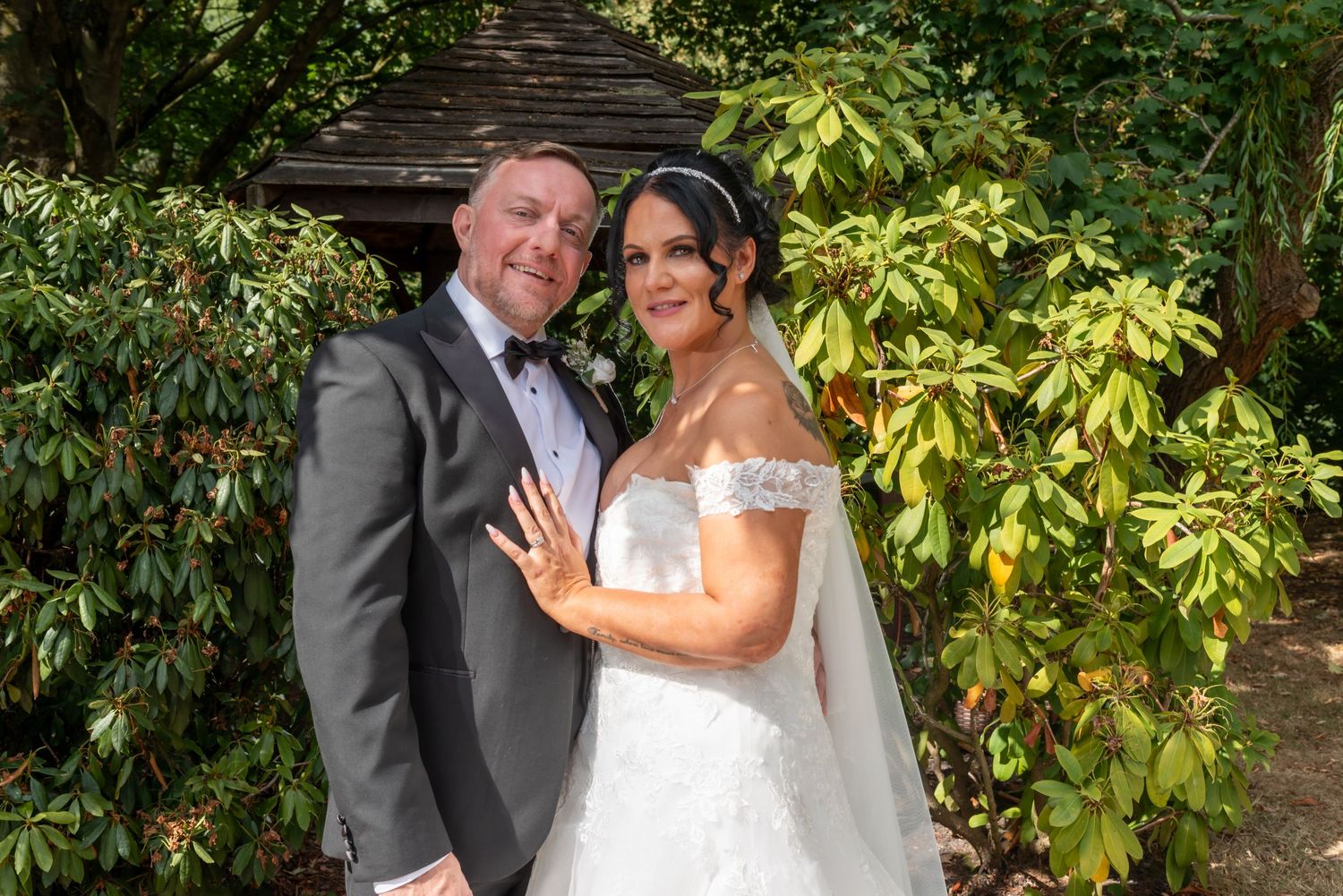 A smiling bride and groom pose together in a lush garden setting on their wedding day.