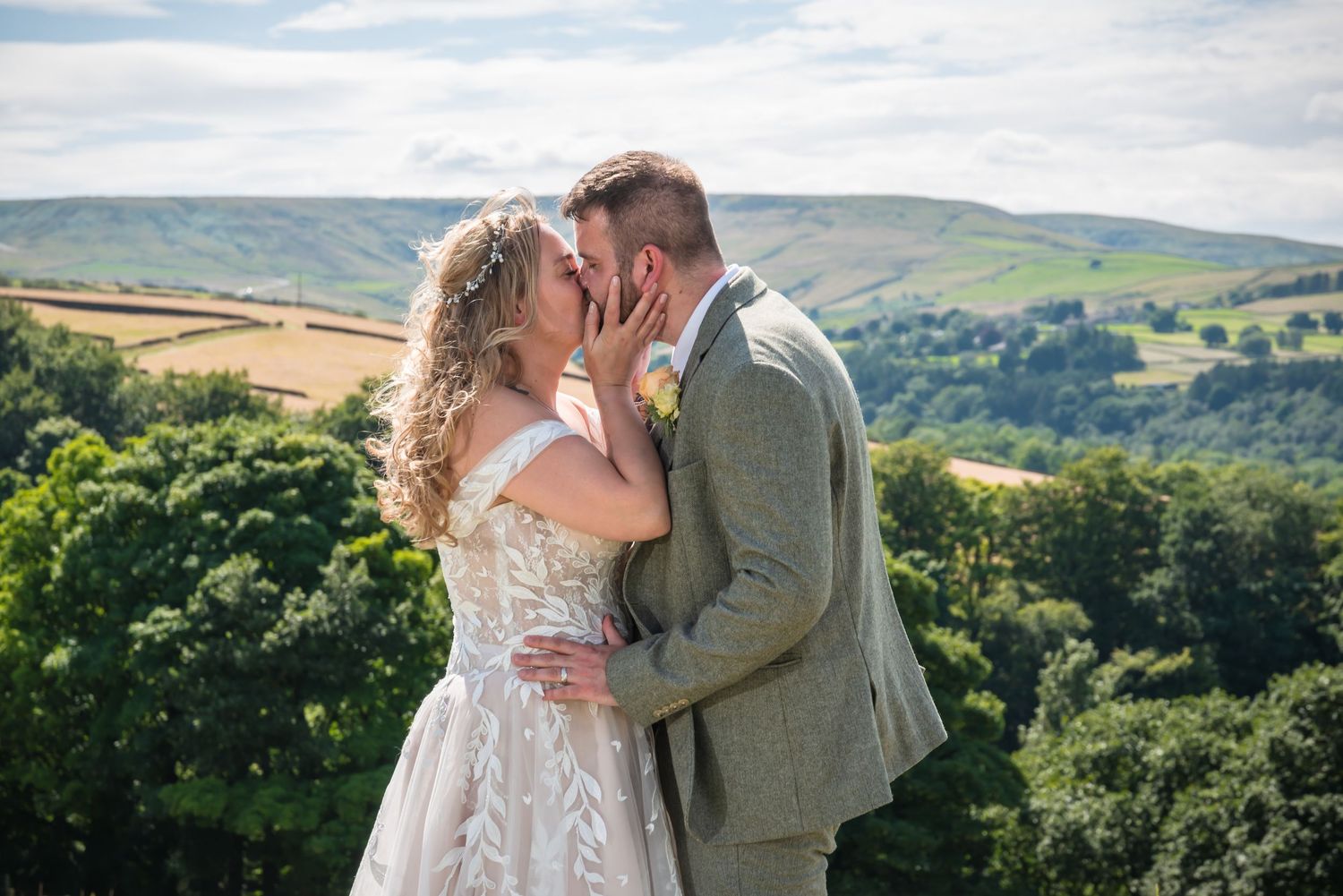 A bride and groom share a romantic kiss at their outdoor wedding with rolling green hills in the background.